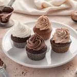 Four chocolate cupcakes with different chocolate frosting styles on a white plate with baking tools.chocolate cake frosting recipes