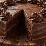 Moist and rich chocolate cake made with Doctored Chocolate Cake Mix with Sour Cream, topped with chocolate ganache and frosting swirls on a wooden stand.