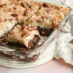 german chocolate poke cake recipe photo 2 with coconut-pecan filling in holes and on top, one square removed showing layers in glass baking dish