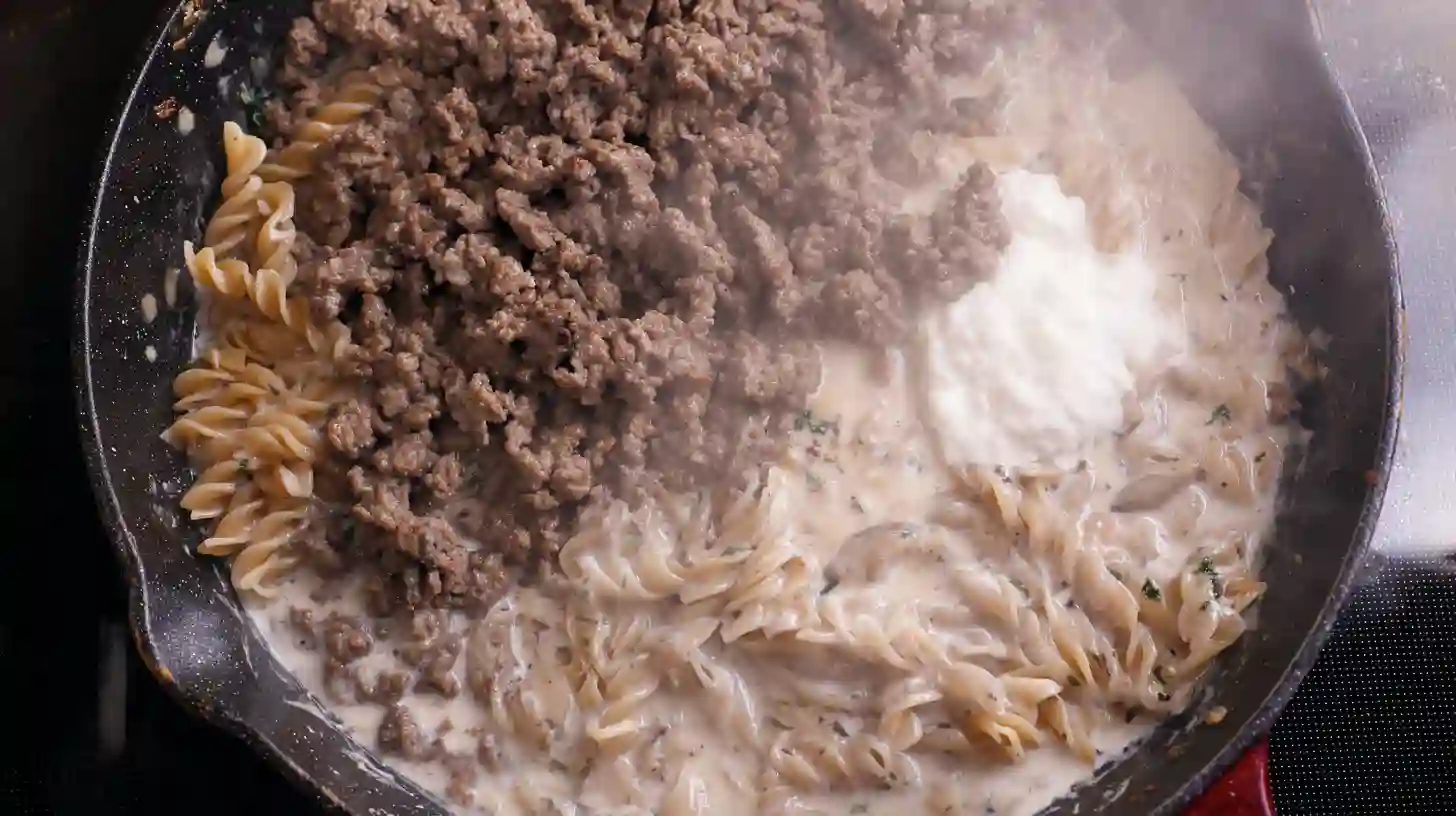 adding-pasta-broth-to-beef-pasta Adding beef broth and pasta to skillet for creamy beef and garlic butter pasta