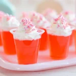 strawberry jello shots with whipped cream and pink sprinkles