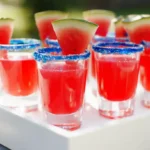 Watermelon Lemon Drop Shots with blue sugar rims and watermelon wedges