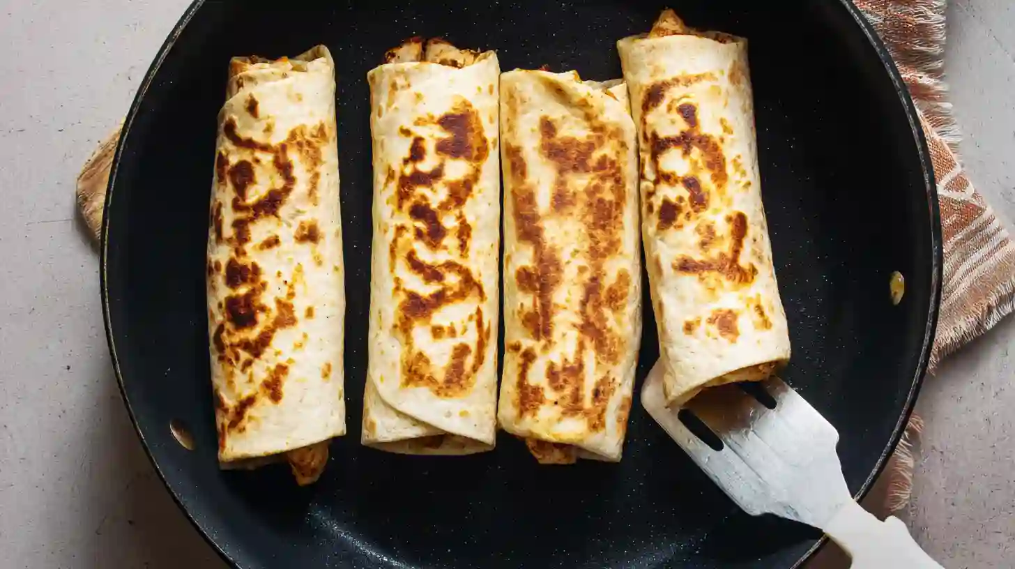crisping-chicken-burritos-in-skillet Chicken burritos being crisped seam-side down in a skillet