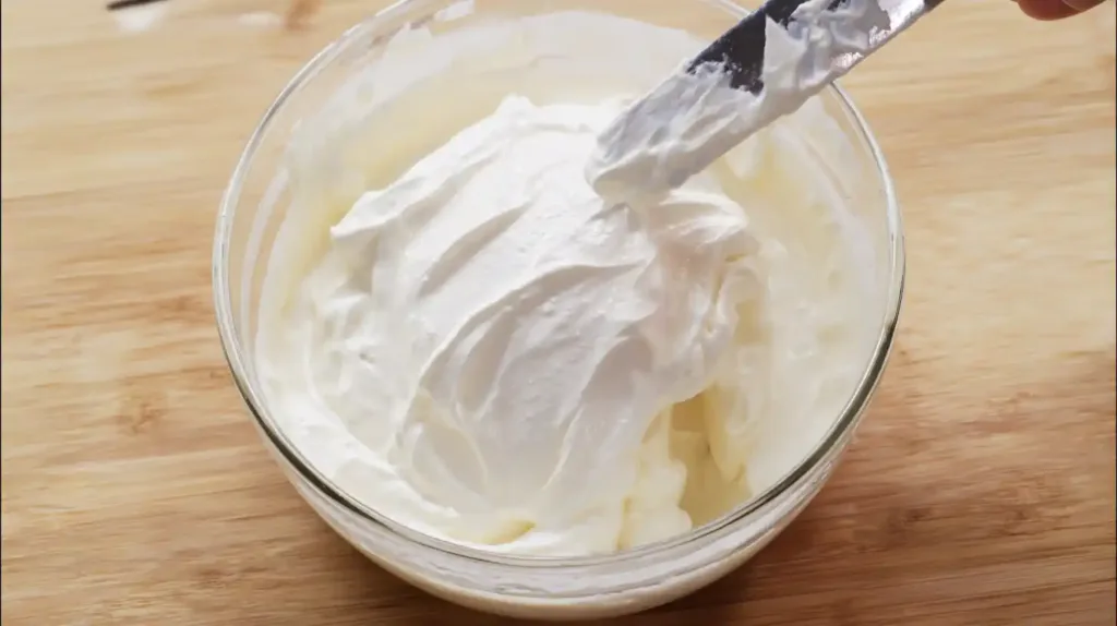 Folding whipped cream into pudding mix for Strawberry Cheesecake Banana Pudding Recipe – easy layered dessert recipes and creamy dessert recipes for families.
