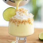 Pouring creamy Key Lime Pie Cheesecake Piña Colada into glass, topped with lime, coconut, and whipped cream – tropical cheesecake cocktail, best summer frozen drinks