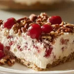 A slice of cherry pecan cheesecake lush with whipped cream layers, bright red cherries, and chopped pecans on top, sitting on a vanilla wafer crust