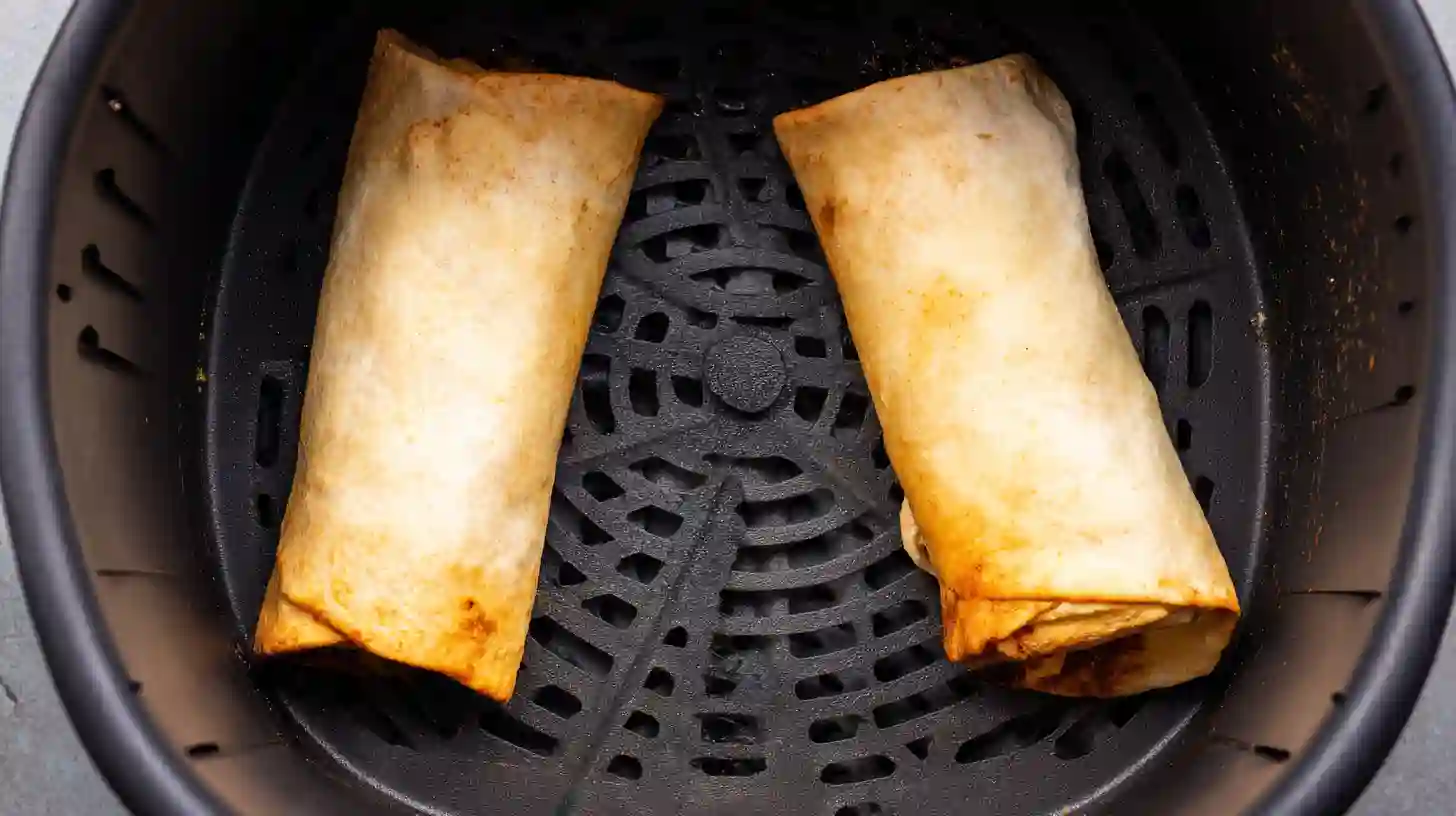 Two golden brown chimichangas sitting inside a black air fryer basket with a crispy dry texture.