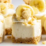 Close-up of cheesecake banana pudding bites with creamy filling and crushed wafer topping, neatly arranged in a clear container under natural light