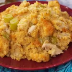 Southern chicken and dressing casserole made with cornbread, shredded chicken, and celery on a red plate — a classic comfort food dish.
