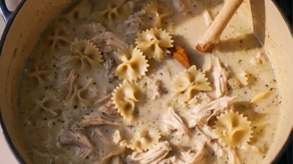 Stirring bowtie pasta and shredded chicken into creamy soup for high-protein chicken recipes and easy comfort food meals.