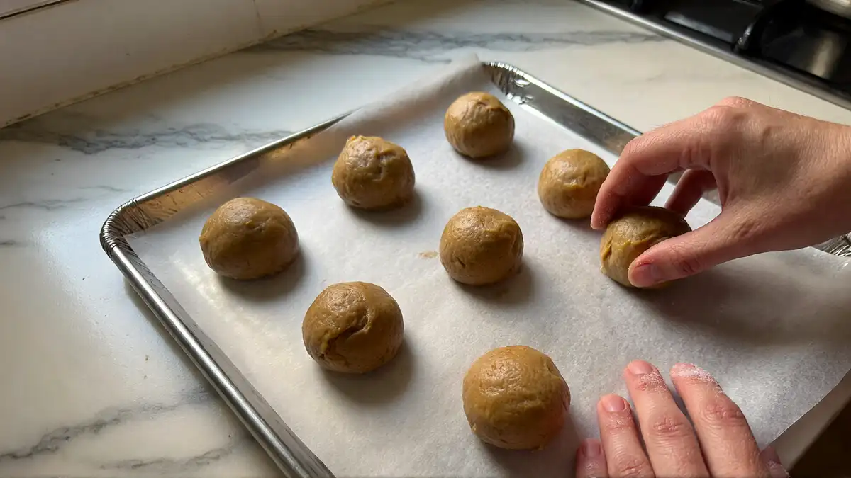Rolling peanut butter cookie dough balls for baking on ungreased cookie sheet — easy beginner cookie recipe without butter.