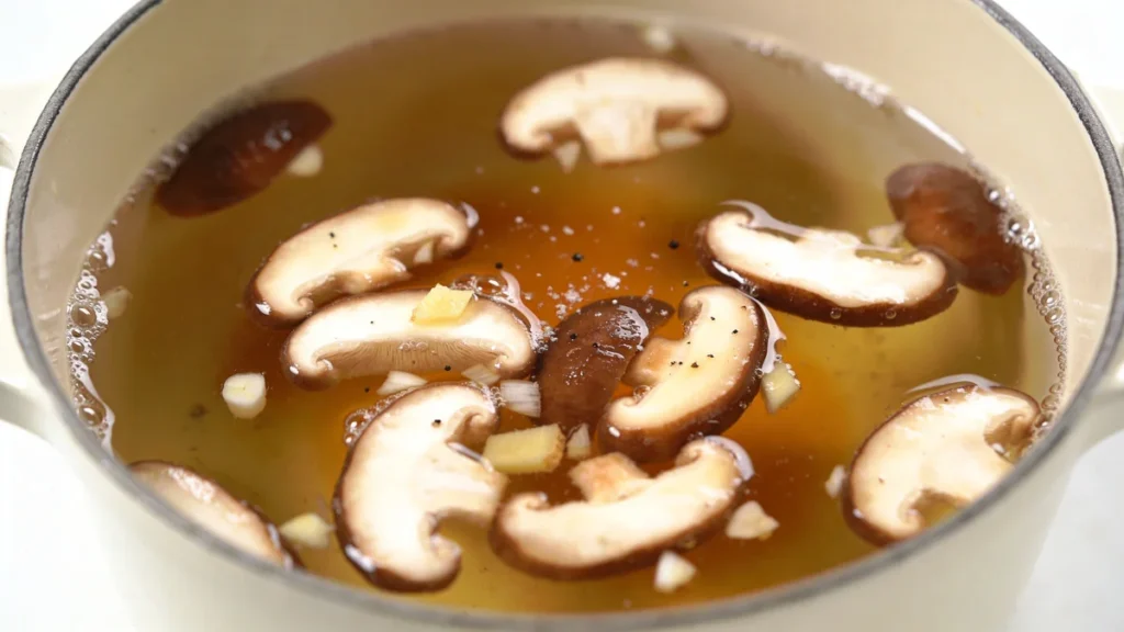Mushrooms simmering in seasoned broth in a pot for Healing Ginger Garlic Broth with Rice Noodles, a healthy homemade soup recipe and easy high protein dinner idea
