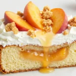 Heavenly summer peach cobbler poke cake topped with whipped cream, fresh peach slices, and golden crumble on white marble — easy homemade peach dessert recipe